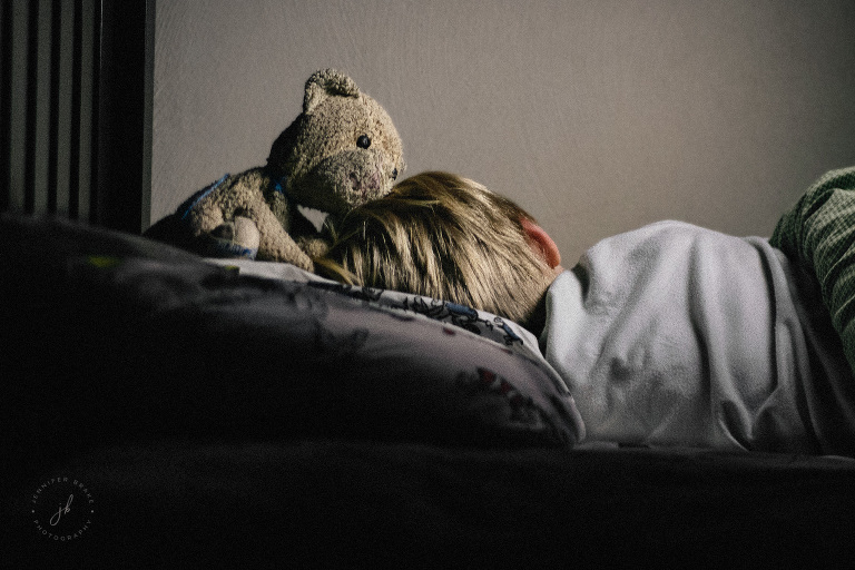 A boy's stuffed cat kisses him tenderly as he sleeps.