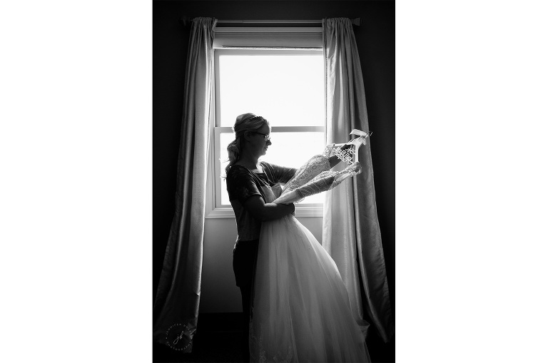 A bride admires her gown, hanging on a whimsical hanger with her married name, before she dons the dress.