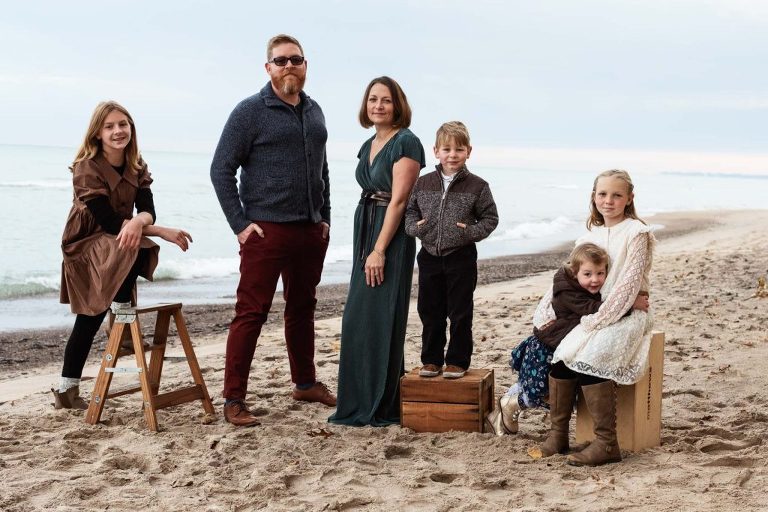 Editorial-style photograph of a family of six on a Lake Michigan beach in the fall. They are dressed in greens, reds, and blues that pop from the coolness of the water and sand around them.