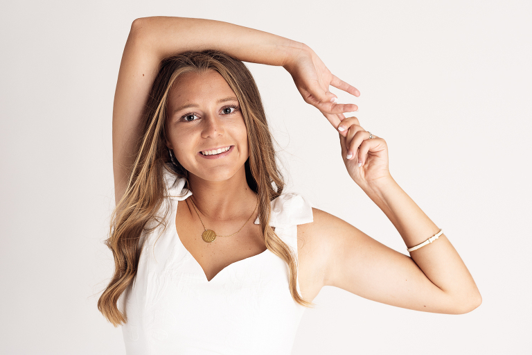 A high school senior girl makes eye contact with the camera as she joins her hands over her head.